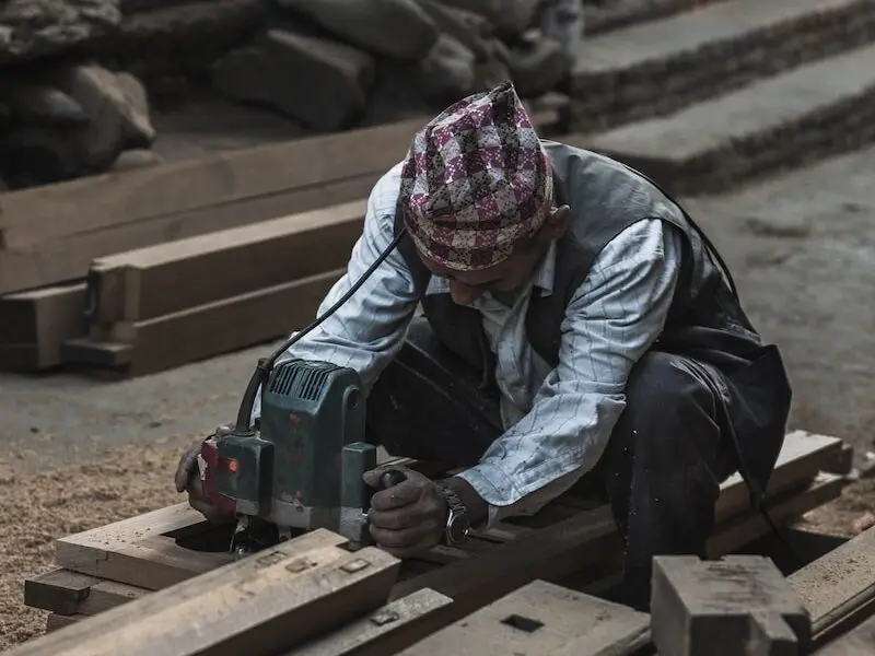 man in white striped shirt sitting on brown pallet holding gray power tool